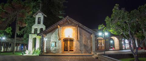 Una iglesia de piedra iluminada por la noche, rodeada de árboles y jardines.