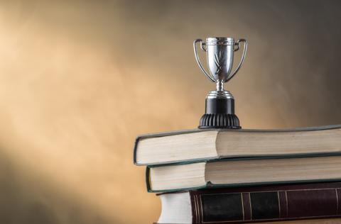 Un trofeo brillante descansa sobre un montón de libros, simbolizando el logro y el conocimiento.