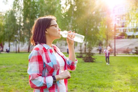 Una mujer bebiendo agua en un parque durante el día.
