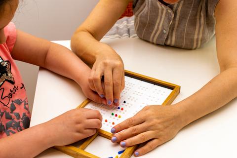 Una niña y una adulta están jugando con un tablero mientras colocan fichas de colores.