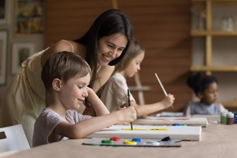 En una clase de arte, una madre sonriente observa a su hijo mientras pinta con entusiasmo.