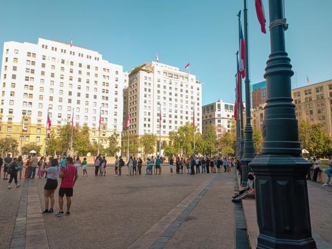 Una plaza en Santiago con mucha gente y edificios altos al fondo.