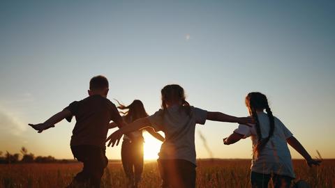Un grupo de niñ@s corre felices hacia el atardecer en un campo abierto.