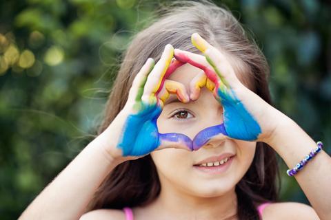 Niña feliz mostrando un corazón con las manos pintadas de colores.