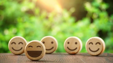 Unos emoticones de madera sonrientes sobre una mesa, en un entorno natural.