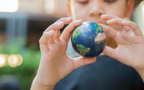 Un niño sostiene una miniatura del planeta Tierra entre sus manos.