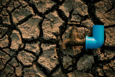 Una llave de agua conectada a una tubería de plástico azul sobre un suelo agrietado por la sequía.