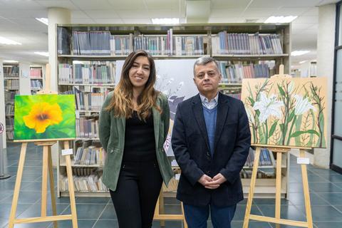 Una mujer y un hombre posan frente a varias obras de arte en una biblioteca.
