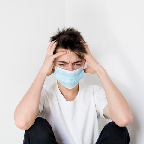 Un joven con mascarilla se muestra angustiado y se agarra la cabeza.