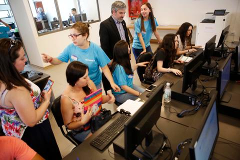 Un grupo de personas jóvenes en un aula informática interactuando y trabajando en computadoras.