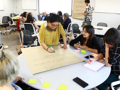 Un grupo de personas discutiendo y escribiendo en una pizarra durante un taller.