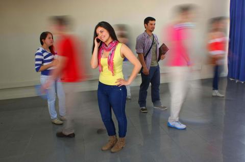 Una joven sonriente habla por teléfono mientras otras personas se mueven de manera borrosa a su alrededor.