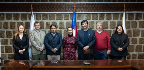 Un grupo de personas posando frente a una bandera chilena en un entorno institucional.