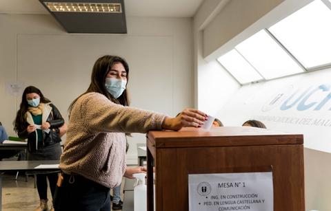 Una mujer vota en una mesa electoral mientras otras personas esperan su turno.