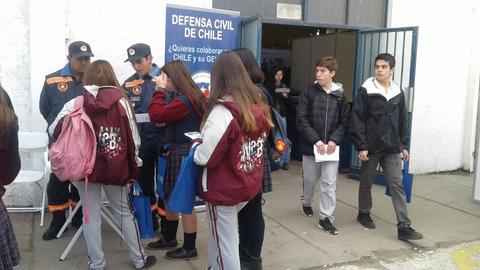 Un grupo de estudiantes interactúa con miembros de la Defensa Civil de Chile en un evento educativo.