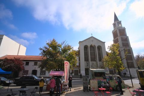Una plaza con un food truck y gente disfrutando del día, al frente de una iglesia en un ambiente tranquilo.