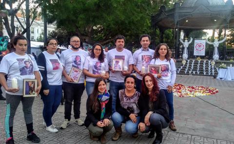 Un grupo de personas se reúne en un evento con camisetas conmemorativas y retratos enmarcados.