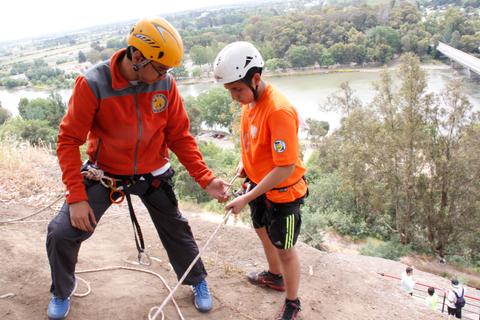 Una persona adulta enseña a un niño las técnicas de escalada en una pared de roca.