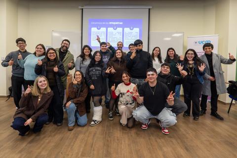 Un grupo de jóvenes sonrientes en un contexto de reunión o actividad educativa, mostrando el pulgar hacia arriba.