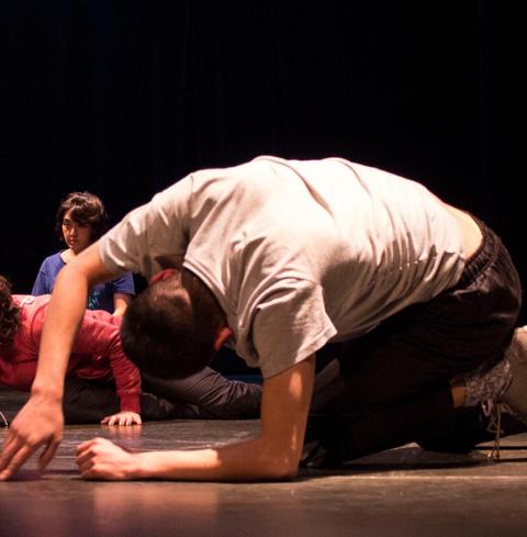 Un grupo de jóvenes se está expresando a través de la danza en un escenario oscuro.