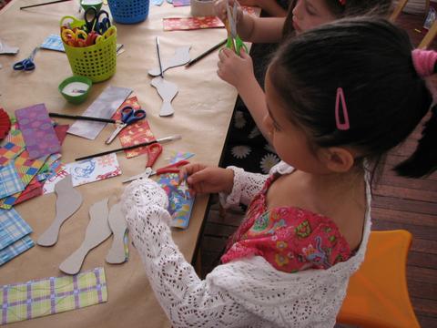 Niñas realizando manualidades con tijeras y papeles de colores en una mesa.