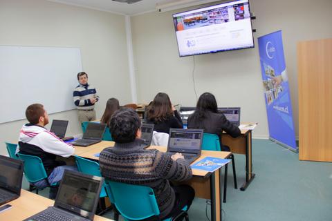 Un grupo de estudiantes asiste a una clase frente a un proyector, utilizando laptops en un aula.