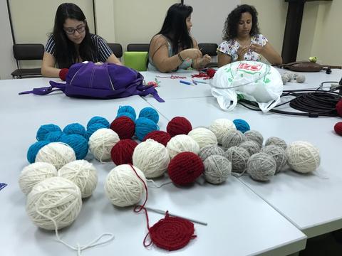 Un grupo de personas se reúne para tejer con ovillos de lana de diferentes colores en una mesa.