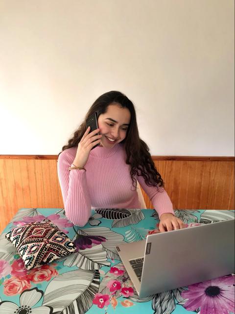 Una joven sonriente está hablando por teléfono mientras trabaja en su laptop en una mesa colorida.