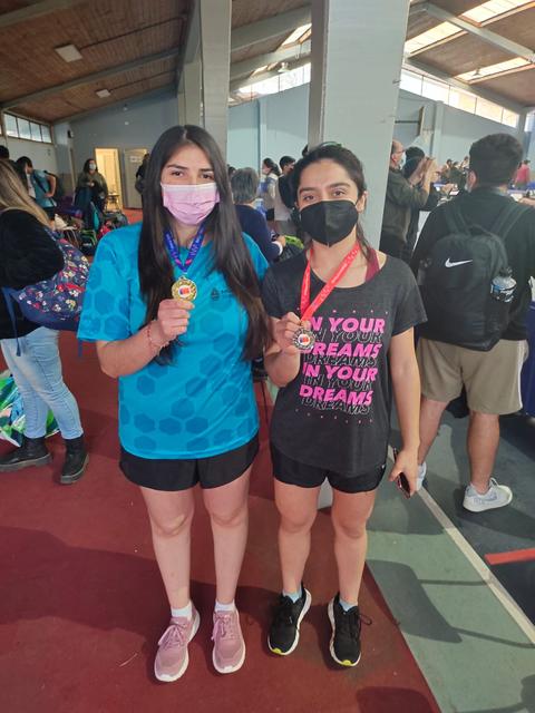 Dos jóvenes atletas posan sonrientes con medallas en un evento deportivo.