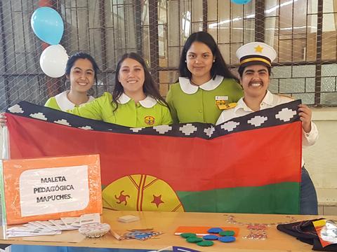 Cuatro mujeres sonrientes posan junto a una mesa decorada con artículos educativos y una bandera mapuche.