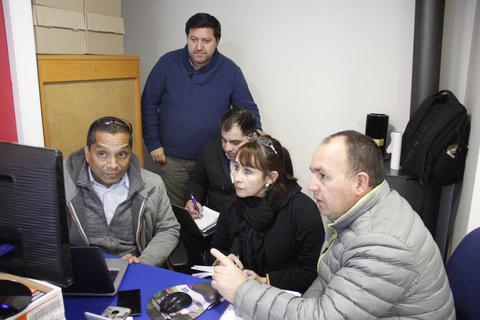 Un grupo de cinco personas conversando y trabajando frente a una computadora en una sala.