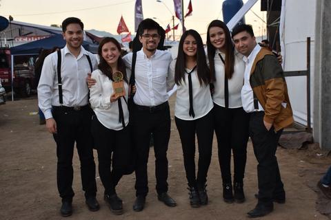 Seis personas posan juntas sonriendo en un evento al aire libre, todos con ropa formal.
