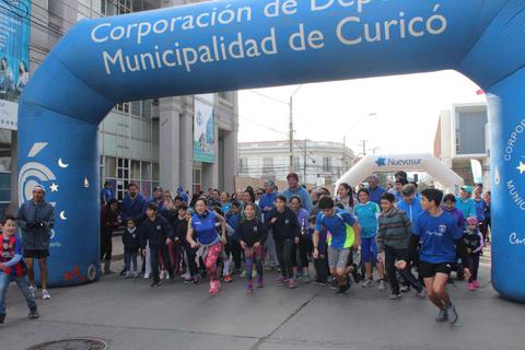 Un grupo de personas, incluyendo niños y adultos, corriendo bajo un arco de inicio en Curicó.