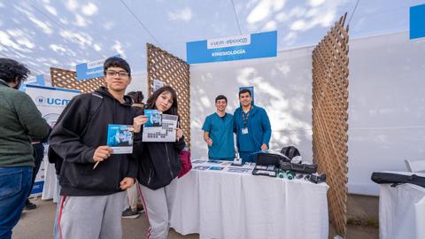 Un grupo de estudiantes sostiene folletos frente a un stand de kinesiología en un evento.