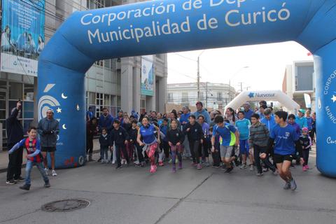 Un grupo de personas participa en una carrera al aire libre bajo un arco inflable de meta en Curicó.