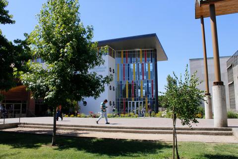 Una moderna edificación con grandes ventanales y colores vibrantes rodeada de árboles y césped.