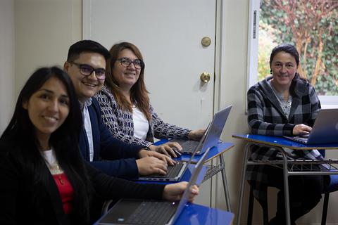 Un grupo de cuatro personas sonrientes trabajando con computadoras portátil en un ambiente iluminado.