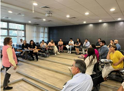 Una presentadora se dirige a un grupo de personas en una sala de clases.
