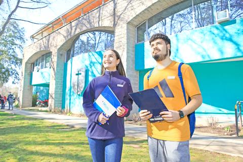 Dos estudiantes caminan por el campus de la universidad en un día soleado.