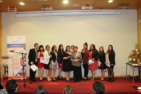 Un grupo de personas posando en un evento formal con un cartel y decoración al fondo.