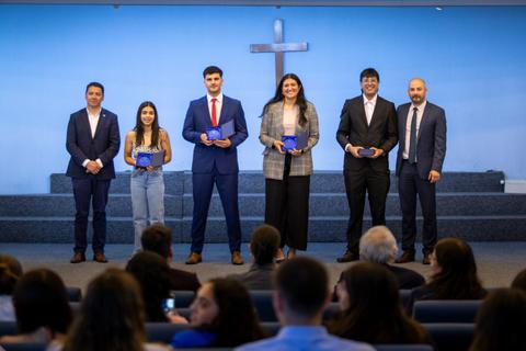 Un grupo de seis personas se presenta en un escenario con una cruz al fondo, sosteniendo premios en las manos.