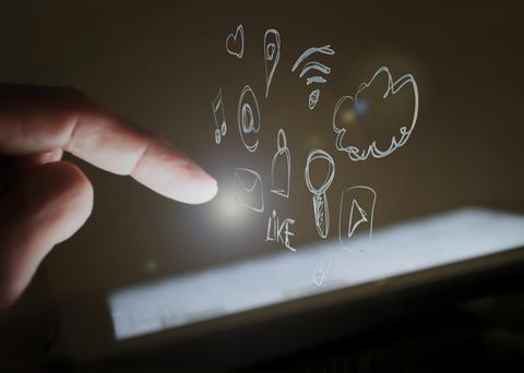 Una mano toca una pantalla iluminada con iconos dibujados que representan redes sociales y multimedia.