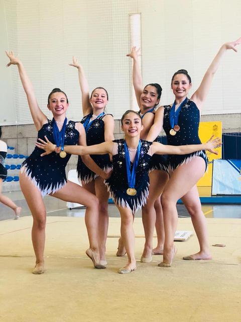 Un grupo de cinco gimnastas posan con medallas en un evento de gimnasia.