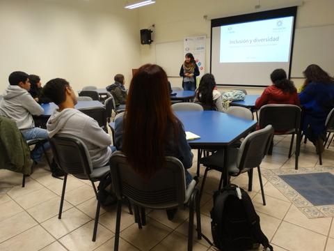 Un grupo de estudiantes escucha a una mujer que presenta un tema sobre inclusión y diversidad en una sala de clases.