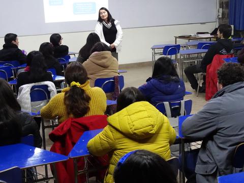 Una mujer está dando una presentación frente a un grupo de personas sentadas en un aula.