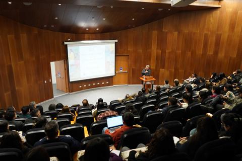 Una charla académica en un auditorio lleno de gente.