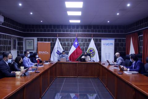 Una reunión formal en una sala de conferencias con varios participantes y banderas de Chile y organizaciones presentes.