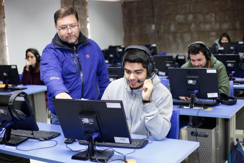Una clase de informática donde un instructor ayuda a un estudiante con su computadora.