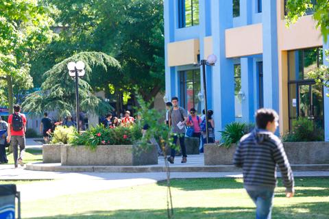 Una escena campus con estudiantes caminando y árboles verdes alrededor de un edificio colorido.