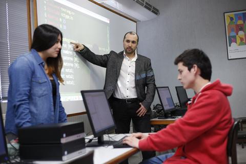 Un profesor explica conceptos de programación a dos estudiantes en un aula de informática.